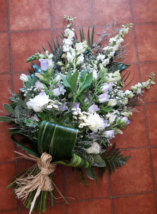 This tied sheaf is in pastel shades flowers include purple Limonium, lilac Campanula, white Delphinium, white Roses, white Gypsophila, white Antirrhinum, Stallion Chrysanthemums with complimentary foliage and a raffia tie