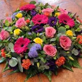 Brightly coloured funeral posy flowers included are yellow spray Roses, pink spray Roses, orange spray Carnations, purple Eustoma, Ageratum and complimentary foliage's.