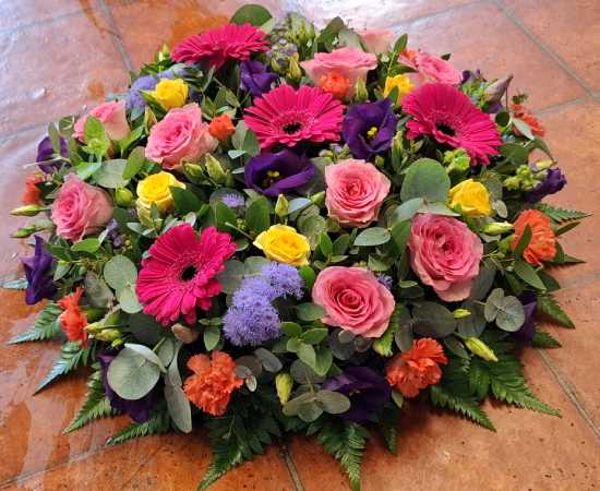 Brightly coloured funeral posy flowers included are yellow spray Roses, pink spray Roses, orange spray Carnations, purple Eustoma, Ageratum and complimentary foliage's.
