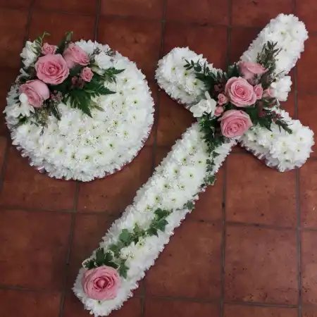 A beautiful mass based cross in white chrysanthemums with a pink ribbon trim and a central spray in pink Roses and white Freesia.