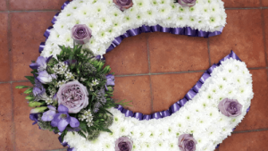 A horse shoe tribute is based with white Chrysanthemums and single roses are placed equally down each side to represent the studs. A spray of flowers added in your chosen colours and a choice of foliage or ribbon for a trim. You can also add a sash with a message or name